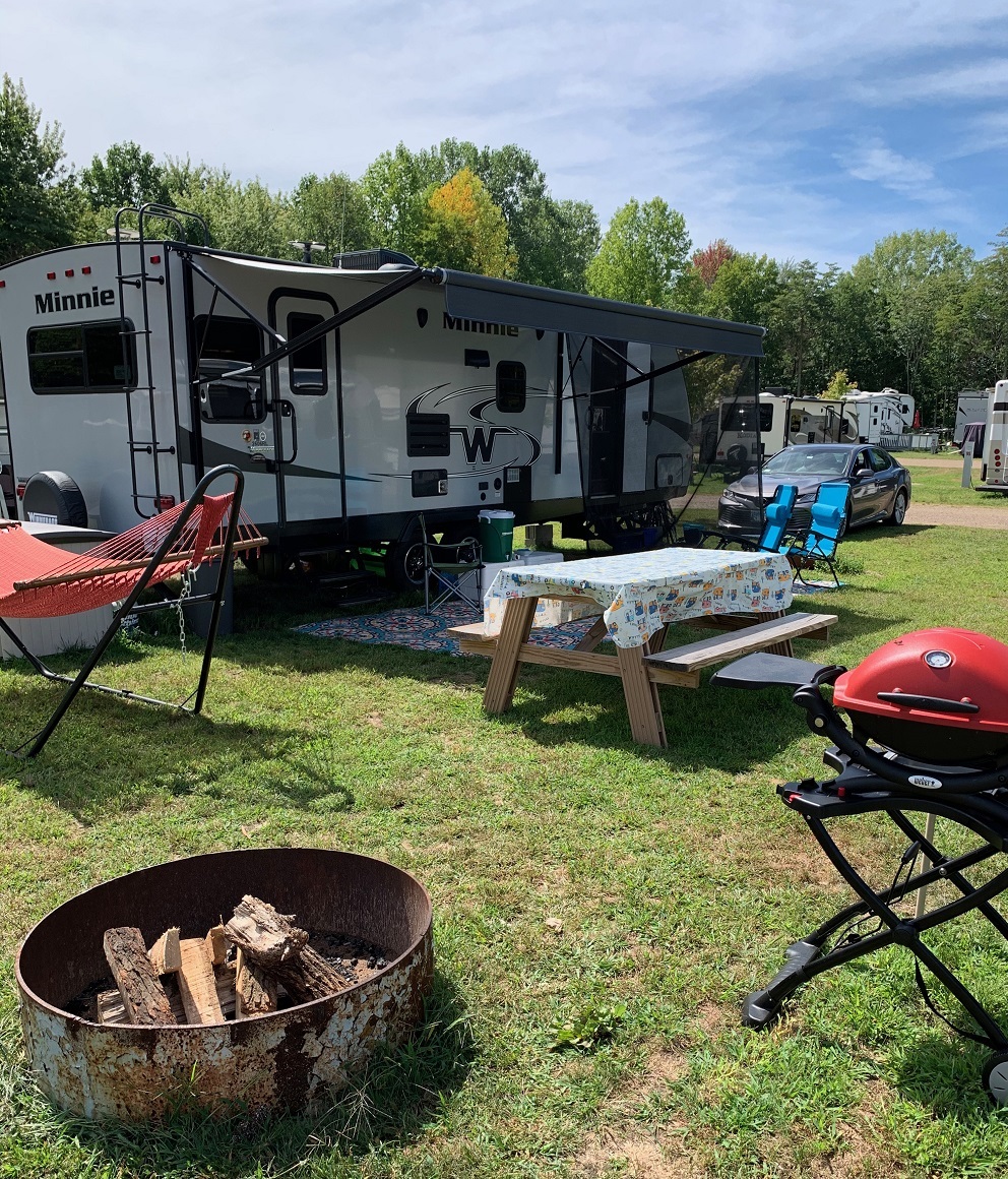  A travel trailer set up with camp at an RV park, set up includes items like a picnic table, grill, and hammock