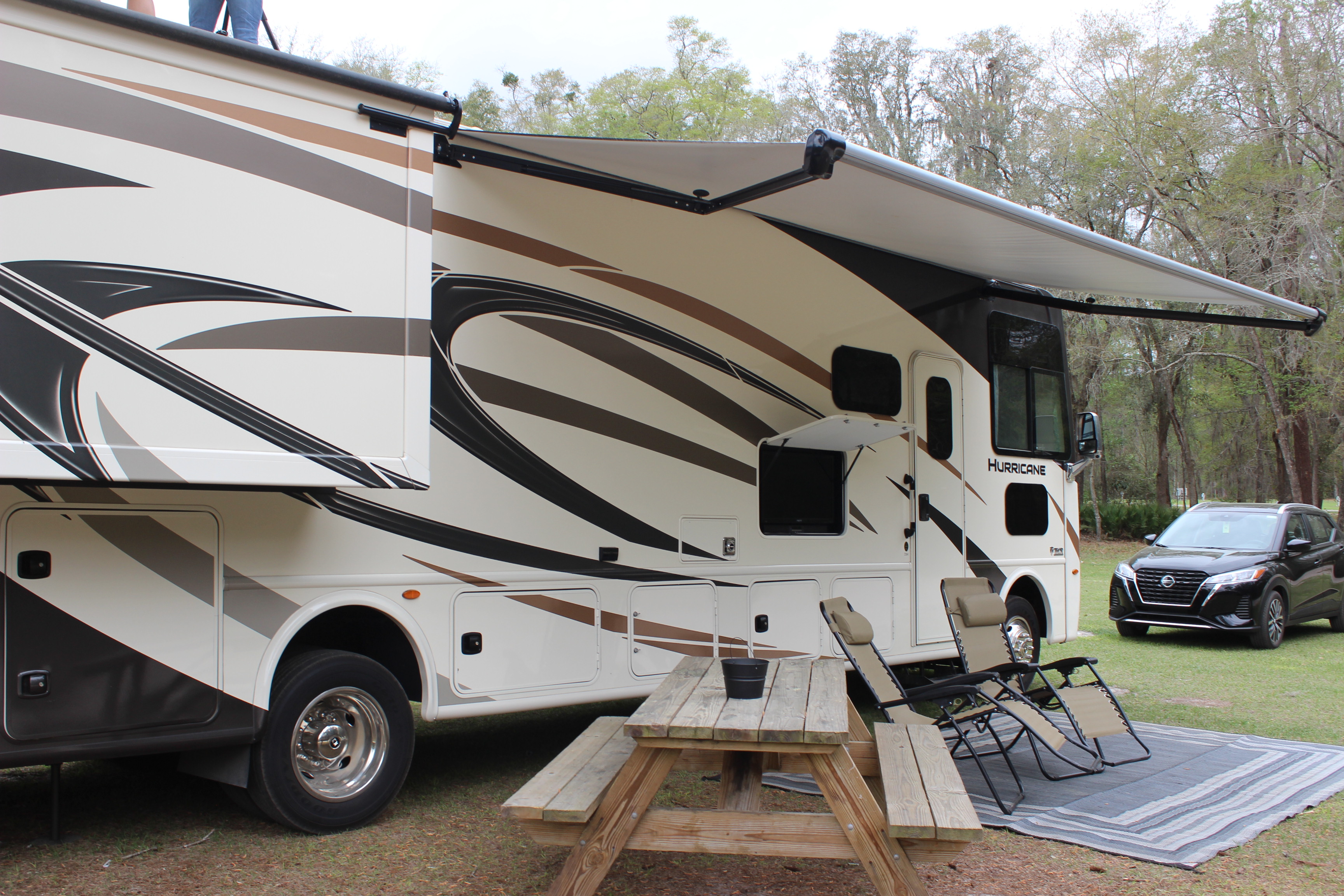 Class A motorhome set up with camp chairs, mat, and table