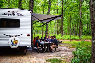 RV in the woods with family eating at the table