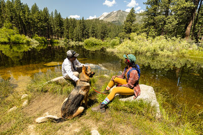 Two people and dog sitting next to river