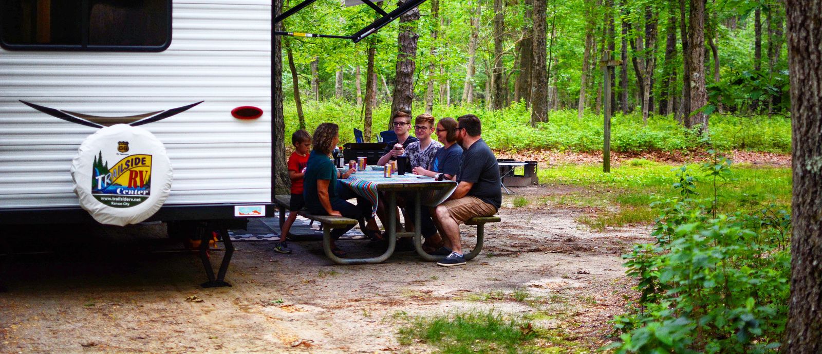 RV in the woods with family eating at the table