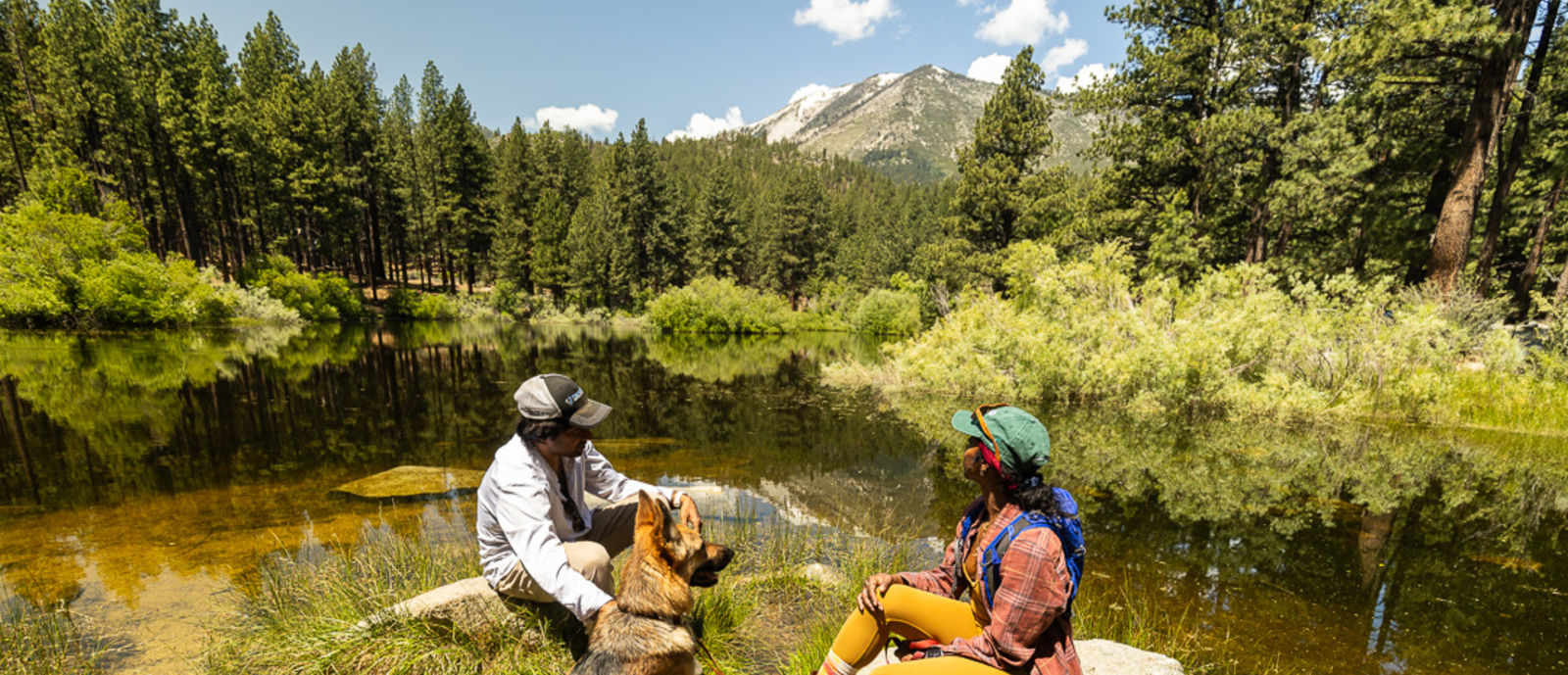 Two people and dog sitting next to river