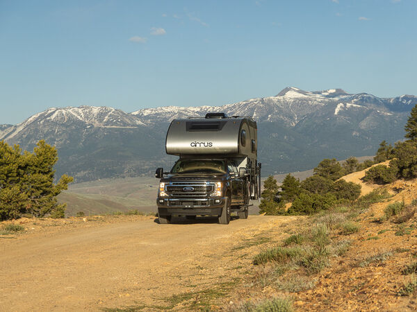 A truck camper drives down a dirt road with the mountains in the background.jpg