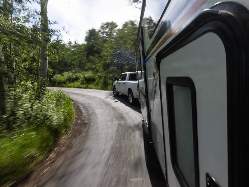 A towable RV travels along a road through the woods.