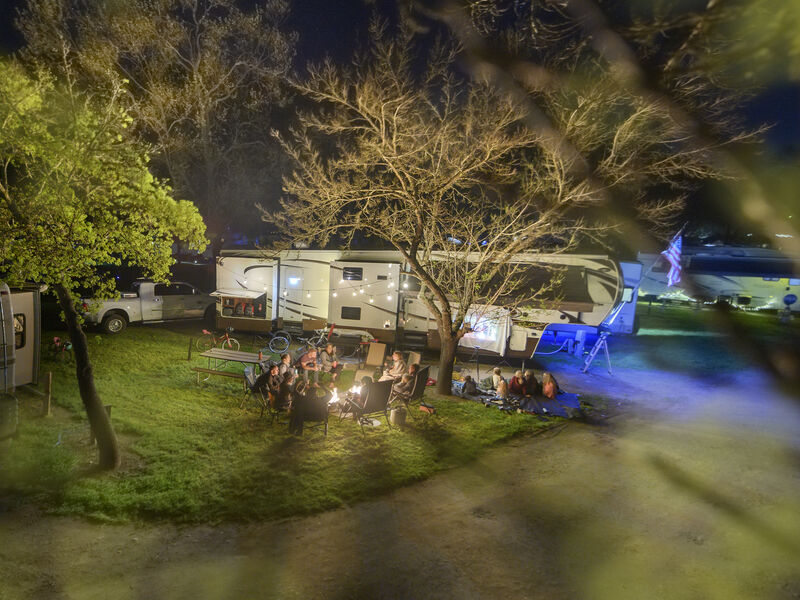 Family sits around campfire next to RV.