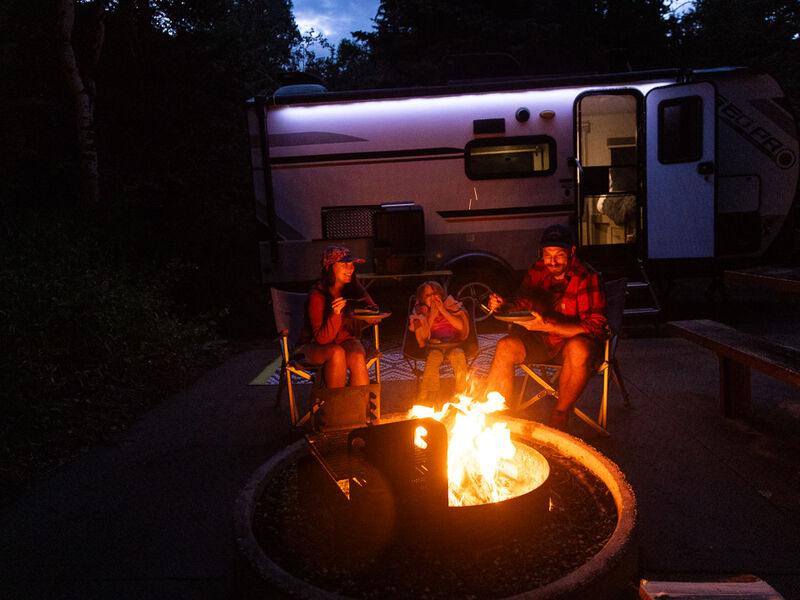 A family gathers around the campfire near their RV