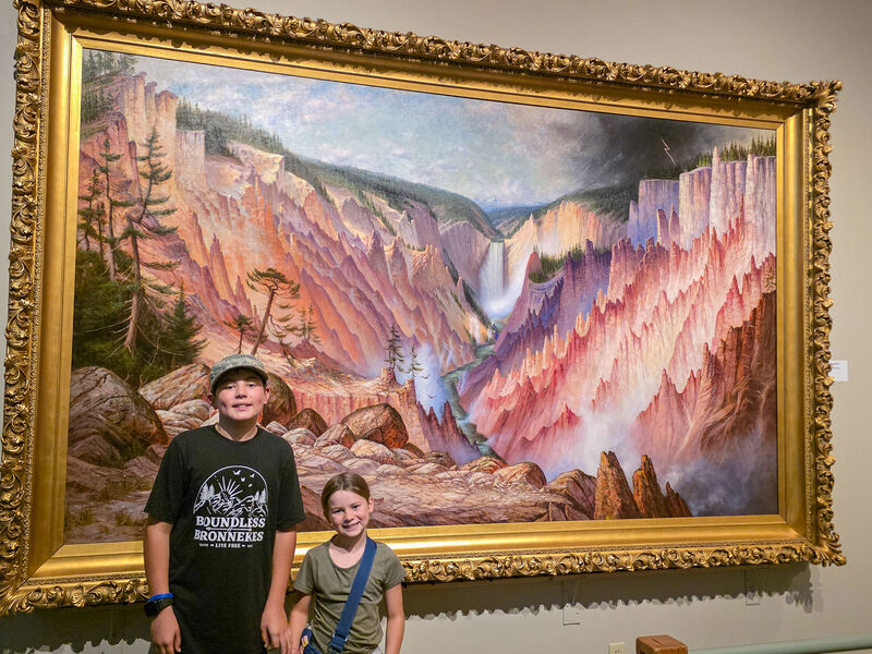 Two children stand in front of a painting in a museum